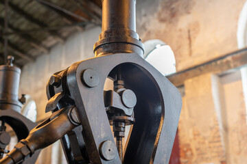 Fragment of steam engine from 1903. Important part of technological line in historical factory. Shabby, devastated walls and arcade window in the background.