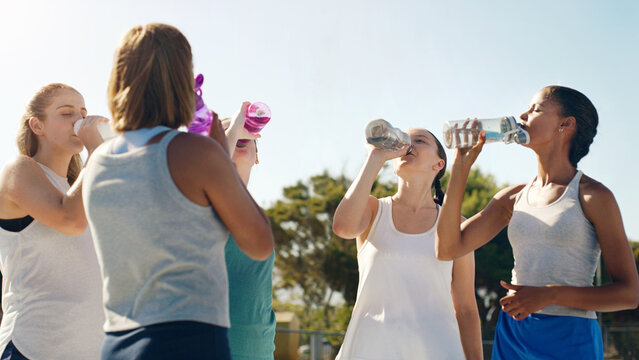 Athletic woman, friends and drinking water for hydration during sports workout, training or practice together outside. Group of sporty women staying hydrated for healthy sport exercise in nature