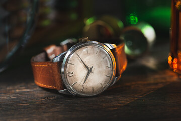 Vintage men's Omega dress watch with white rustic dial and brown leather strap laying on the dark brown rustic wooden table near to the instruments.
