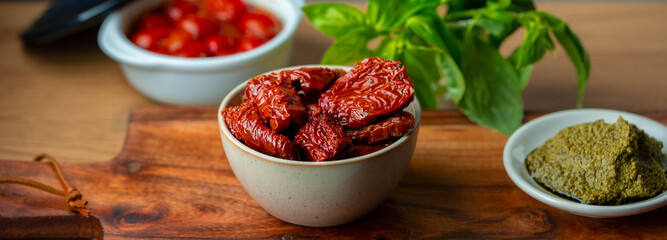 Bowl of sun dried tomatoes on wooden background.Dried tomato. Sun dried tomatoes. Infinite depth of field. Sun dried tomatoes with fresh herbs and spices. Slate background.Autumn seasonal pickled 