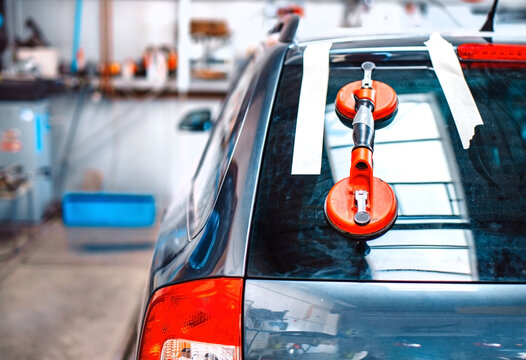 Automechanic is replacing windshield  of a car in auto service station garage.