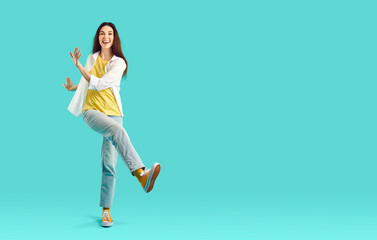 Fototapeta na wymiar Funny millennial girl in casual wear have fun dancing on blue studio background. Smiling young woman make dancer moves enjoy good mood. Hobby and entertainment. Copy space.