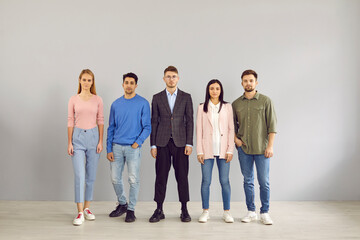Group portrait of young people in smart casual clothes. Team of 5 unsmiling corporate employees in jumpers, jackets, shirts, trousers and jeans standing in studio. Work dress code in office concept