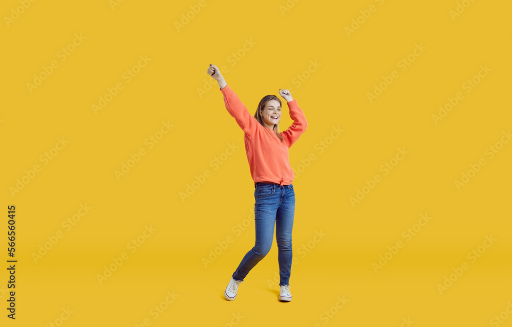 Wall mural Cheerful joyful teen girl in casual clothes having fun and dancing on isolated on yellow background. Grl in sneakers, jeans and sweatshirt rejoices and laughs out loud. Full height. Banner. Copy space