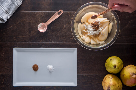 Cropped image of hand adding sugar and coco powder on guava slices in bowl at table