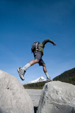 African American hiker jumps over rocks.