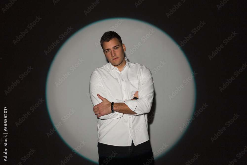 Wall mural Stylish young successful handsome business guy in a fashion white shirt stands in the studio on a circular light on a dark background