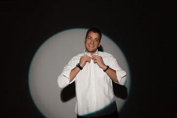 Happy handsome fashionable man professional businessman with a smile in a fashion white shirt buttoning up a button on a dark background in the studio