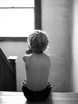 Boy Sits At Top Of Stairs And Looks Out Window