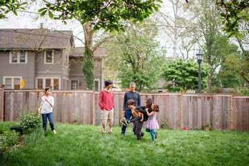 Two brothers play with their children in a suburban fenced-in backyard