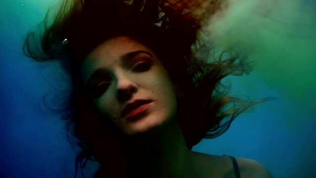 art shot underwater, a woman swims like a drowned man and exhales smoke, slow-motion portrait in the water