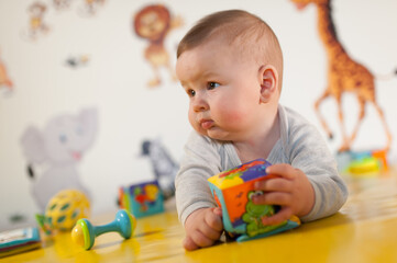 Portrait of cute baby boy playing with colorful toys at home. Close-up view of cute baby boy lies on its stomach and plays with toys. Playground for babies