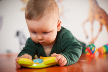 Portrait of cute baby boy playing with colorful toys at home. Close-up view of cute baby boy lies on its stomach and plays with toys. Playground for babies