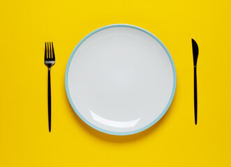 Empty white plate with spoon and fork on yellow background. Meal preparation concept.