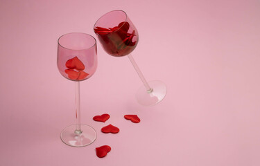 Fototapeta na wymiar Two glass glasses on a pink background filled with red hearts. The concept of love, family, loyalty