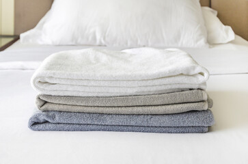 pile of three folded terry towels lies on clean white bed. Cleaning in room of hotel, laundry