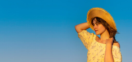 woman in a yellow dress and a hat   on a hill in summer sunset against the blue sky