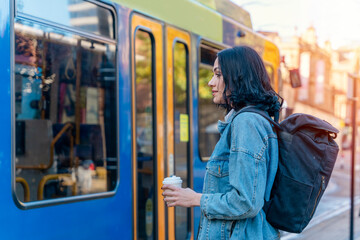 a sad young woman in a denim jacket is talking on the phone and waiting for a tram at the stop Lifestyle photo - obrazy, fototapety, plakaty