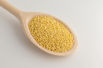 Yellow millet in wooden spoon on a white background