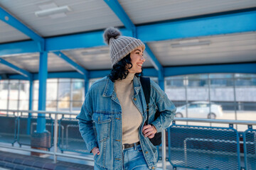 Obraz premium a young woman in a denim jacket is talking on the phone and waiting for a tram, bus at the stop Lifestyle photo