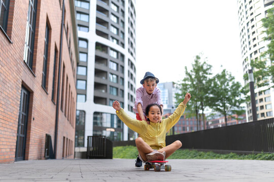 Happy Children Enjoying Skateboard Ride And Going Down The Hill, Looking At Camera.