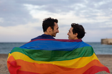Beautiful gay young couple embraces and holds a rainbow flag. Happy couple enjoy at the beach