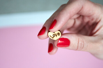 A woman's hand holds a wooden heart with the inscription love in her hands. 