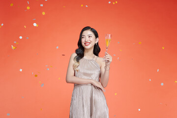 Beautiful stylish woman in holiday outfit holding champagne against the red background of confetti