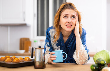 Obraz na płótnie Canvas Sleepy woman in housecoat drinking morning coffee in kitchen