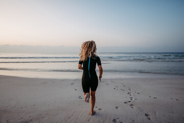 Rear view of woman in neoprene running in to ocean. - Powered by Adobe