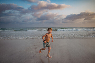 Little boy in swimsuit running out of sea, enjoying holiday.