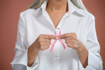 Close-up of senior woman holding pink bow. Breast cancer awareness concept.