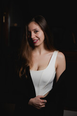 Fototapeta premium The portrait of young sensual brunette caucasian woman in white top, black jacket and bright make up smiling, dark background 