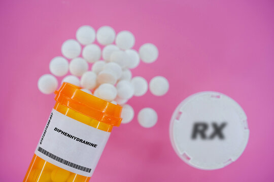 Diphenhydramine Rx medicine pills in plactic vial with tablets. Pills spilling   from yellow container on pink background.