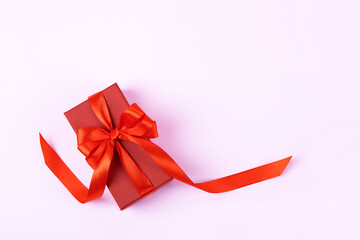 Red gift box with a red satin ribbon bow on a lilac background. Happy Valentine's Day, Mother's Day and birthday greeting card.
