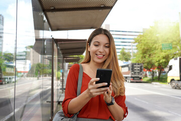 Positive smiling girl buying ticket online with smartphone at bus stop