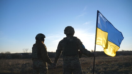 Ukrainian army soldiers stands outdoor at sunset time and waves flag of Ukraine. People in military...