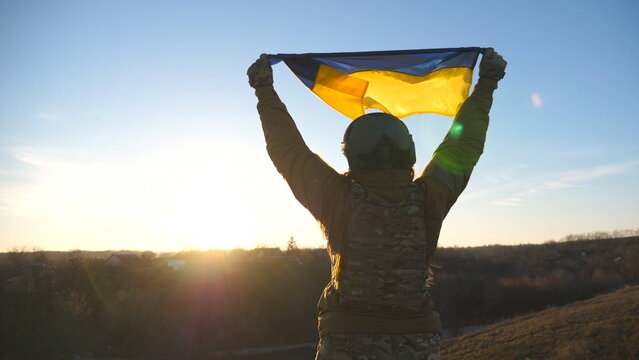 Female soldier of ukrainian army runs to the hill top to wave flag of Ukraine. Woman in military uniform lifted up flag against sunset as sign of victory against russian aggression. Slow motion