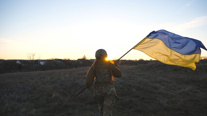 Female ukrainian army soldier runs and waves flag of Ukraine at sunset. Woman in military uniform...