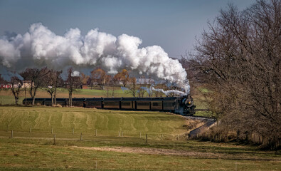 Fototapeta na wymiar A View of An Antique Passenger Train Approaching, Blowing Smoke and Steam, on an Autumn Day