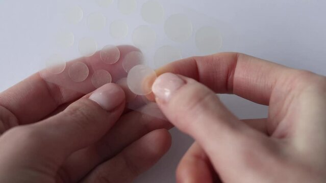 Round patches for acne and wrinkles on the hands on a white background. Acne and wrinkle patches for facial rejuvenation. Cleansing cosmetology. Woman's hand takes one transparent sticker.