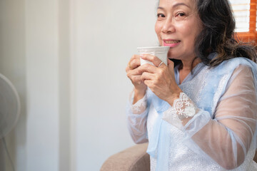 An elderly woman sits and relaxes on the sofa at home, sipping a cup of healthy tea. happily and emotionally relax inside the house on working days off healthy tea concept