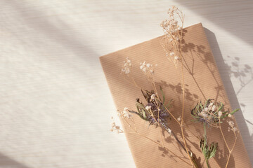 Books and dried flowers on a light wood table lit by the evening light through the curtains