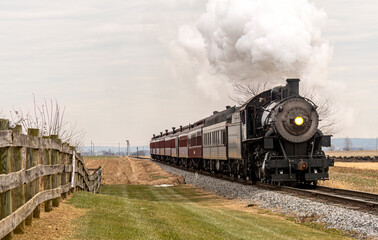 Naklejka premium A View of a Classic Steam Passenger Train Approaching, Traveling Thru the Countryside, on a Winter Day