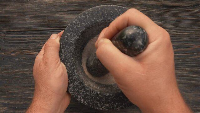 Hand grinding spices in the grey stone mortar 