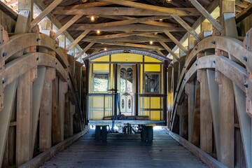 Installing a New Yellow Passenger Antique Coach Thru a Cover Bridge on to a Railroad Track on a Fall Day