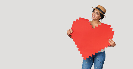 Mixed race girl in straw hat holding big paper pixel style heart shape with copy space for text