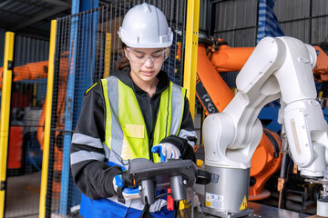 Young female asian service engineer holding robot controller operate robot arm automation factory