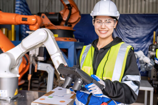 Young female asian service engineer holding robot controller operate robot arm automation factory
