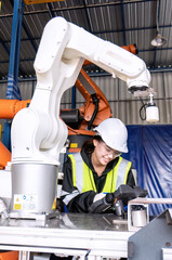 Young female asian service engineer holding robot controller operate robot arm automation factory